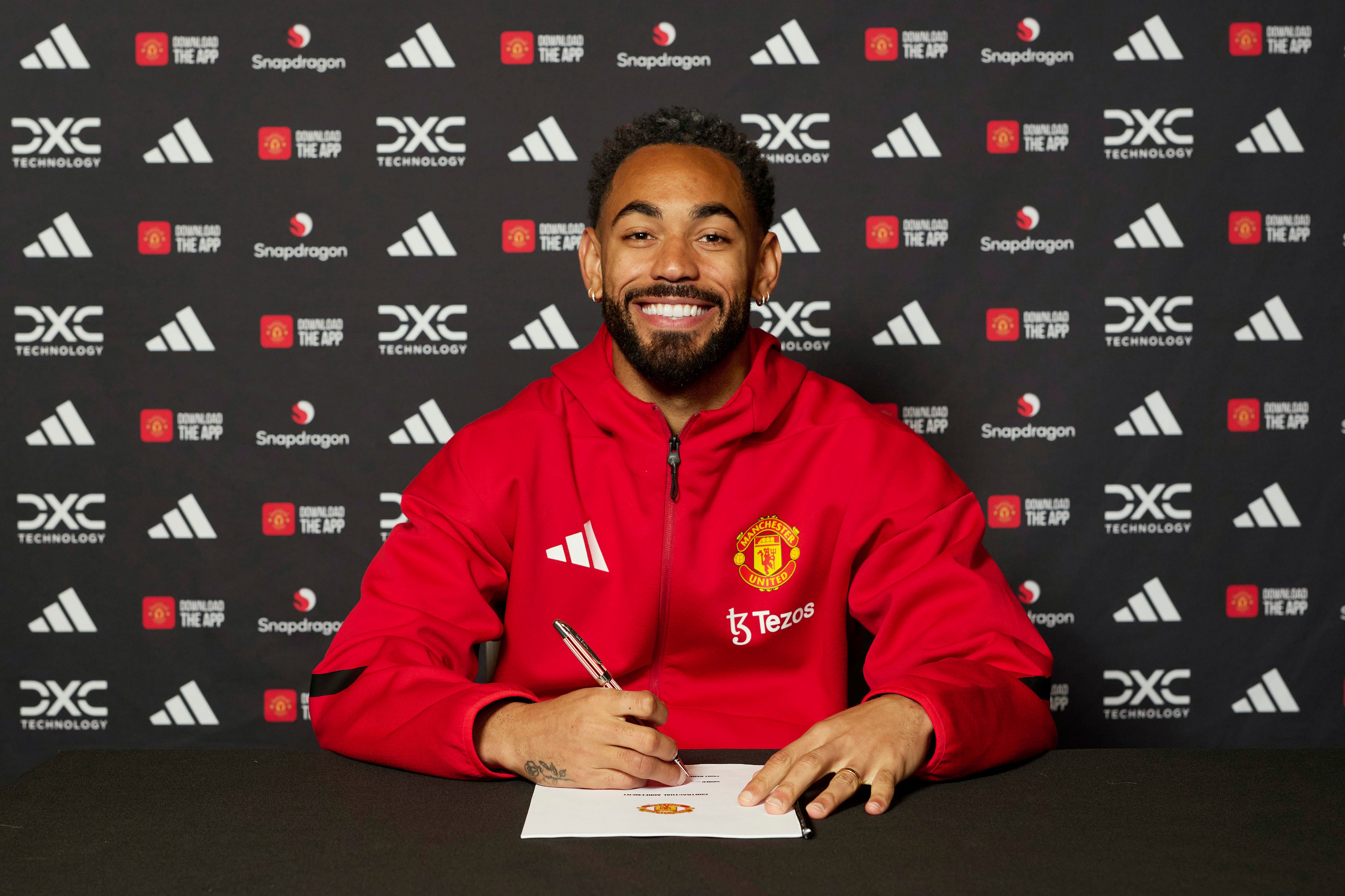 Matheus Cunha smiles while signing his Man United contract.
