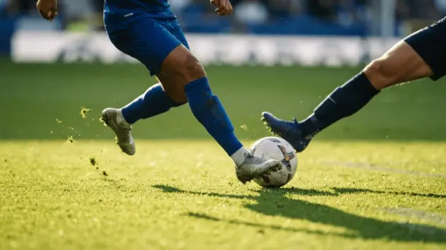 Premier League winger dribbling past defender on football pitch in golden hour light