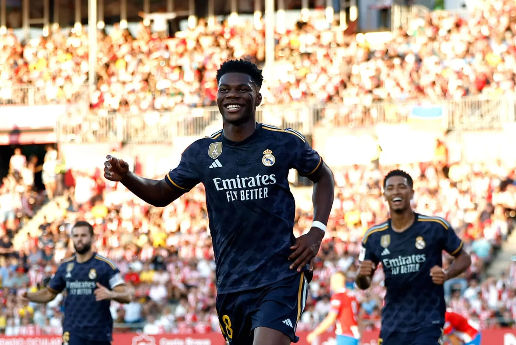 Aurelien Tchouameni smiling in a Real Madrid navy blue kit during a match with crowds in the background