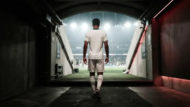 Young footballer in white kit walking through stadium tunnel toward bright lights