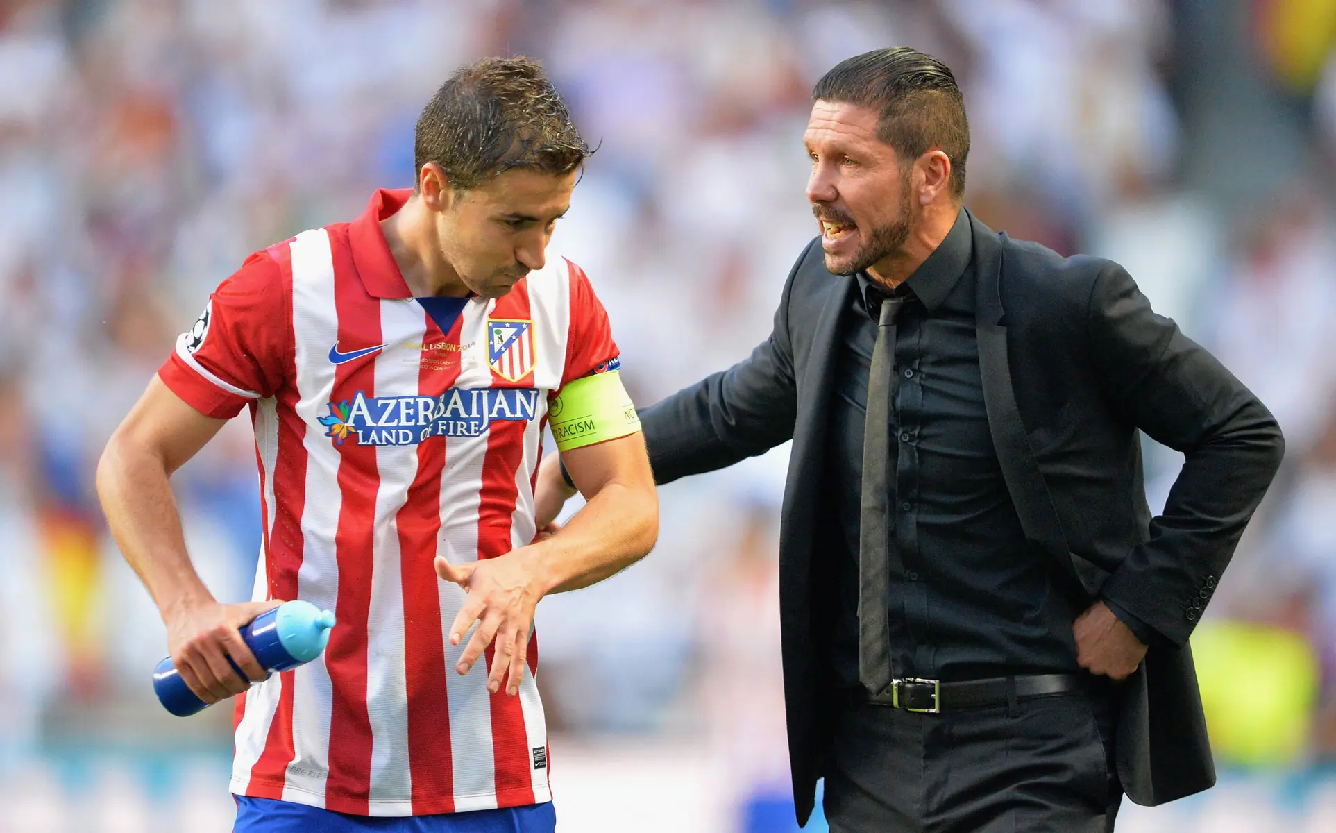 Diego Simeone in a black suit speaking to an Atletico Madrid player in a red and white striped kit