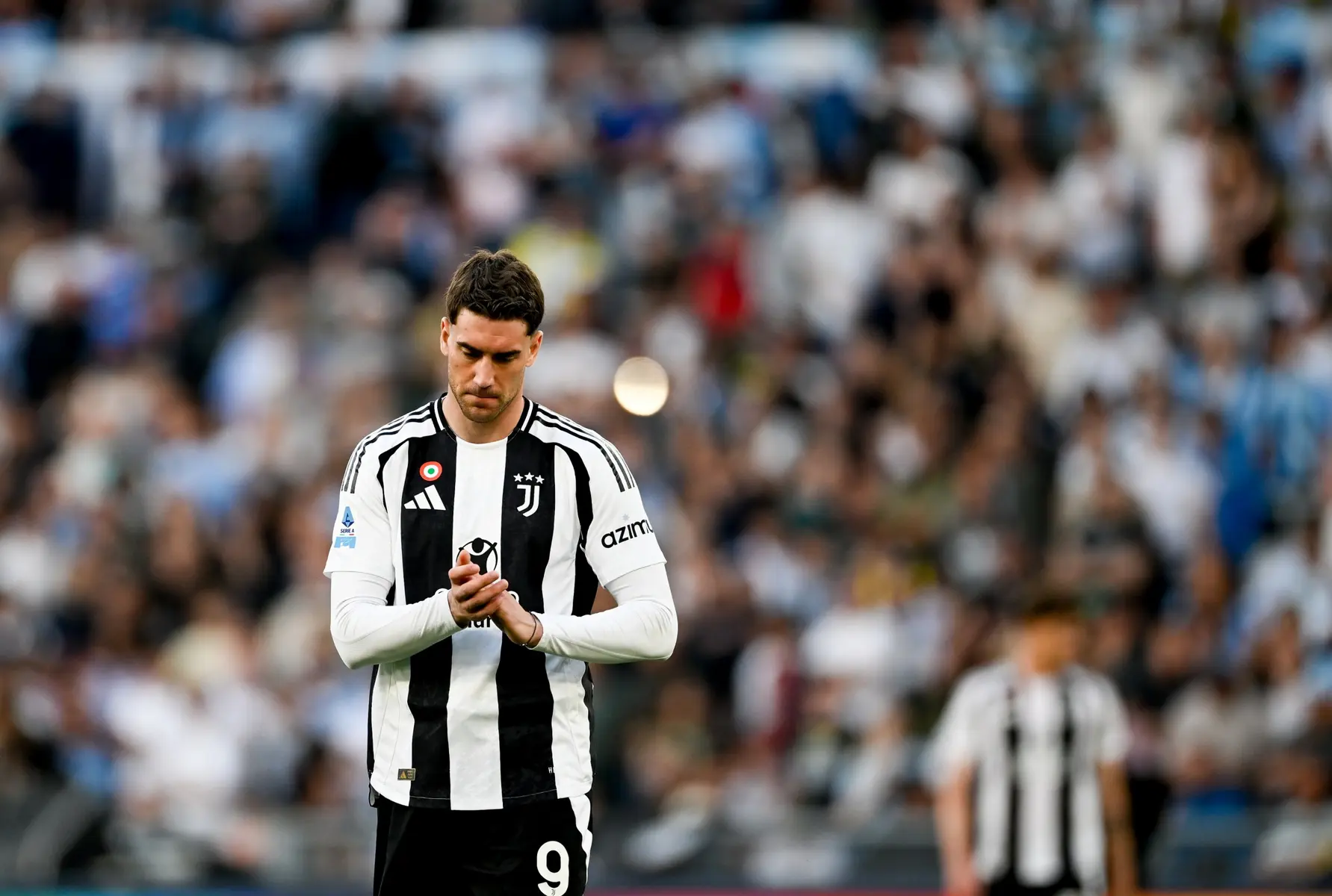 Dušan Vlahović in a Juventus black and white striped jersey standing on a football pitch during a match.