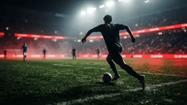 Football winger sprinting with ball on illuminated pitch with red and black dramatic lighting