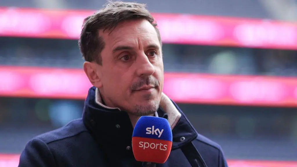 Gary Neville speaking into a Sky Sports microphone at a stadium