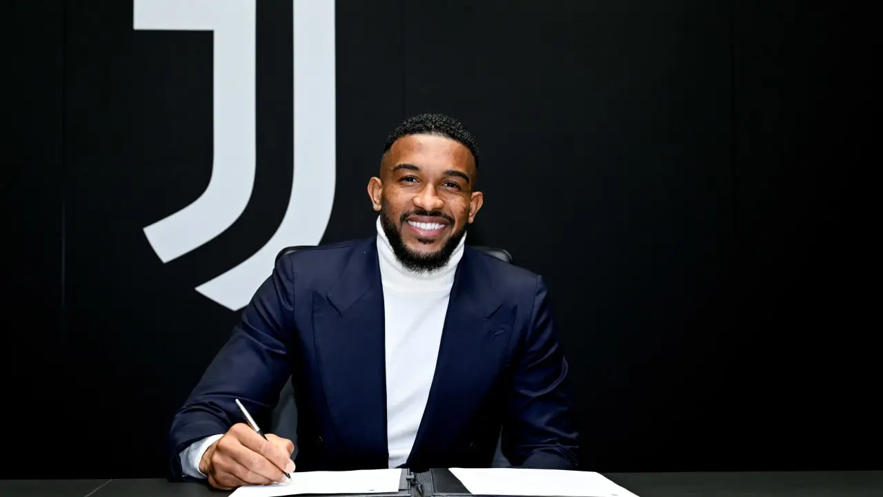 Grayson Bremer sorri ao assinar documentos, com o logotipo da Juventus ao fundo.