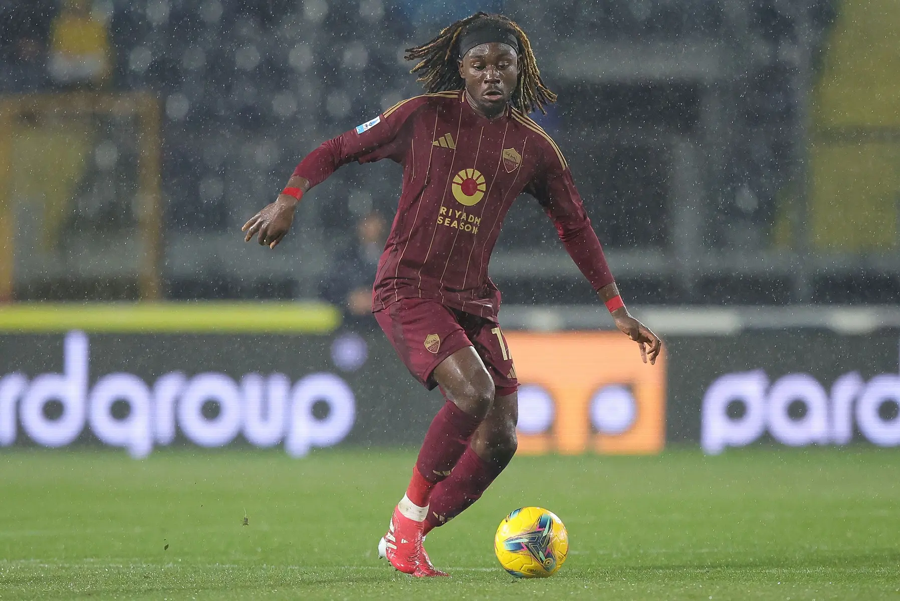 Manu Kone dribbling a soccer ball during a match in rain, wearing a Roma kit.