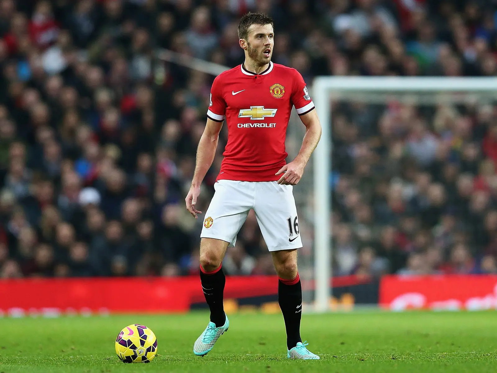 Michael Carrick in a red Manchester United home kit standing on a football pitch with a yellow ball