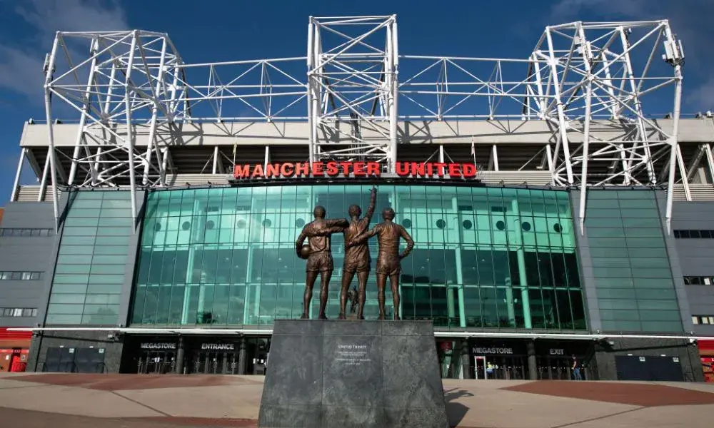 The United Trinity statue of Best, Law, and Charlton in front of the Old Trafford stadium facade