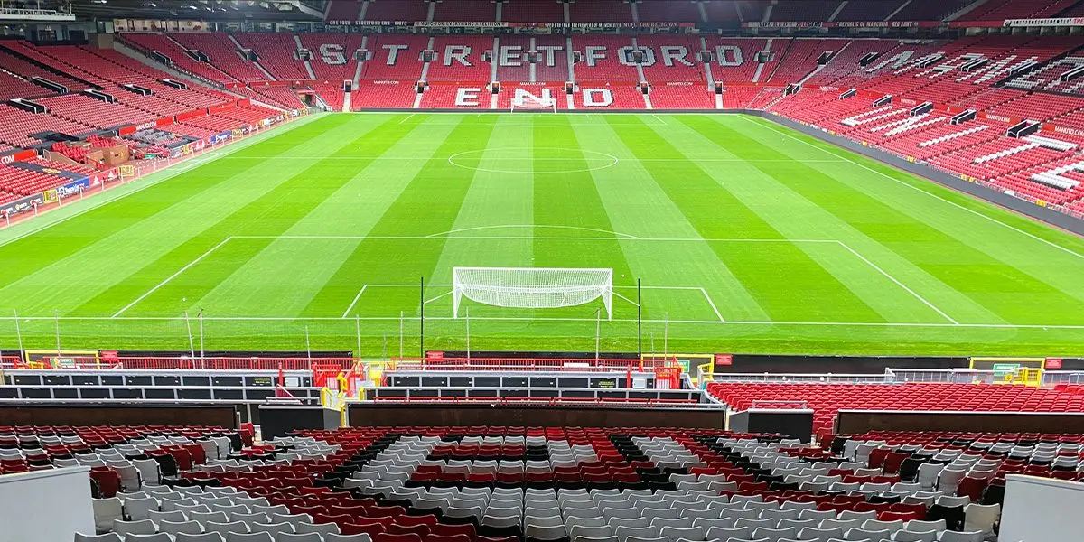 View of the Old Trafford pitch with vivid green grass and empty red seating areas.