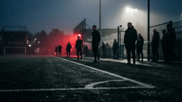 Silhouetted figures on football training ground with dramatic red accent lighting and stadium backdrop