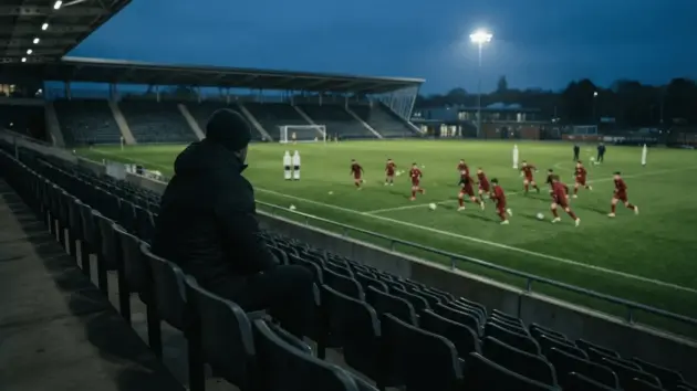 Coach silhouette watching youth players train on Manchester United pitch from stadium stands
