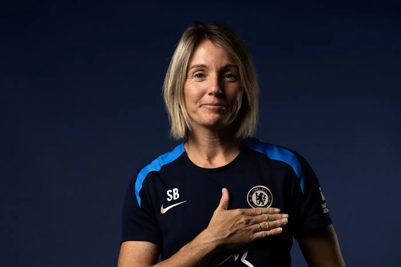 Sonia Bompastor in a Chelsea shirt, smiling and gesturing with one hand.