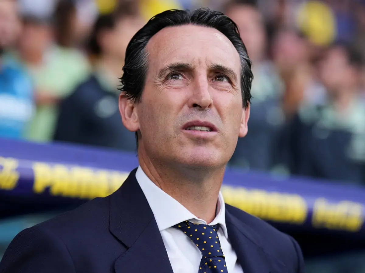 Close-up portrait of Unai Emery wearing a dark suit and a blue tie with yellow polka dots.
