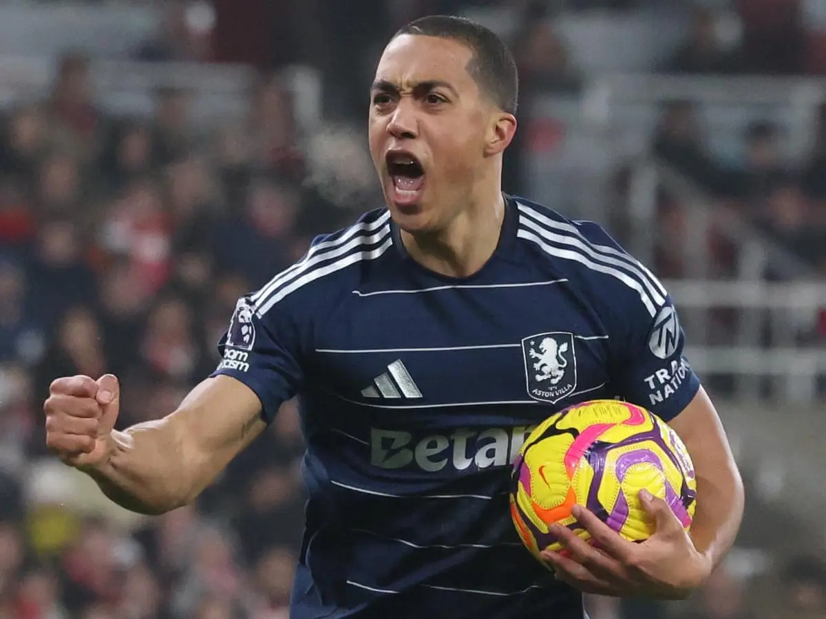 Youri Tielemans in an Aston Villa kit celebrating while holding a yellow and purple soccer ball