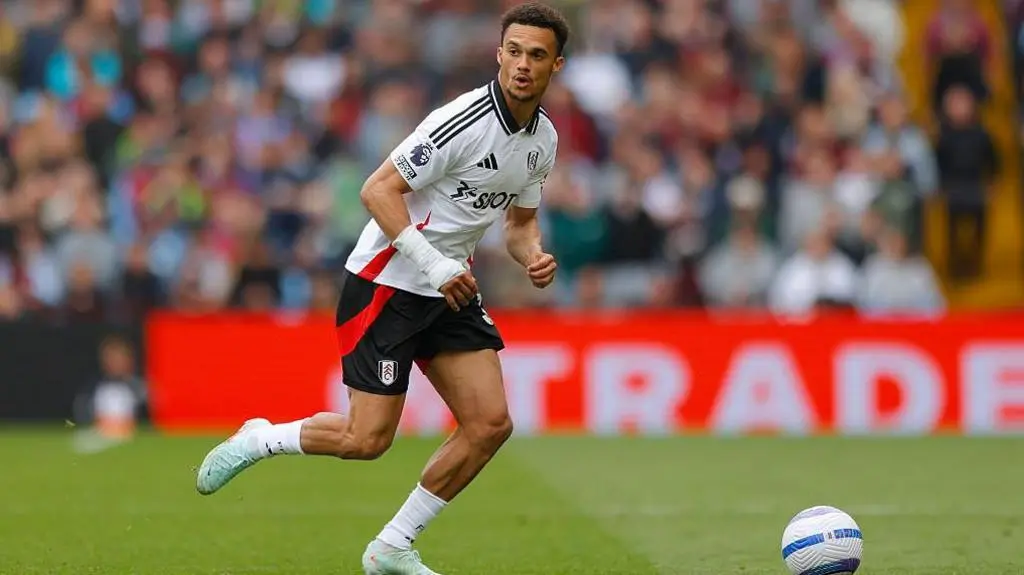 Antonee Robinson in a white Fulham FC kit running with a football on a grass pitch
