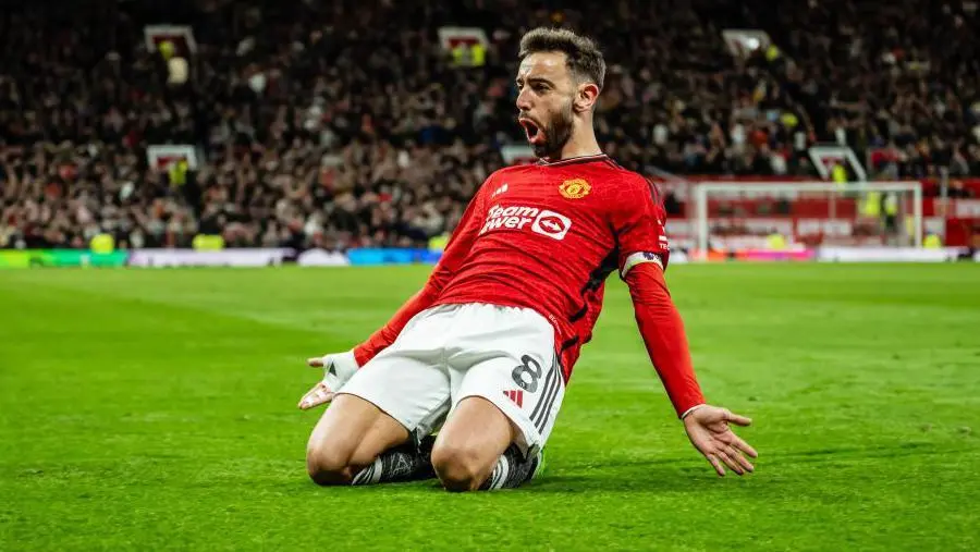Bruno Fernandes celebrating on his knees in a Manchester United home kit on a grass pitch