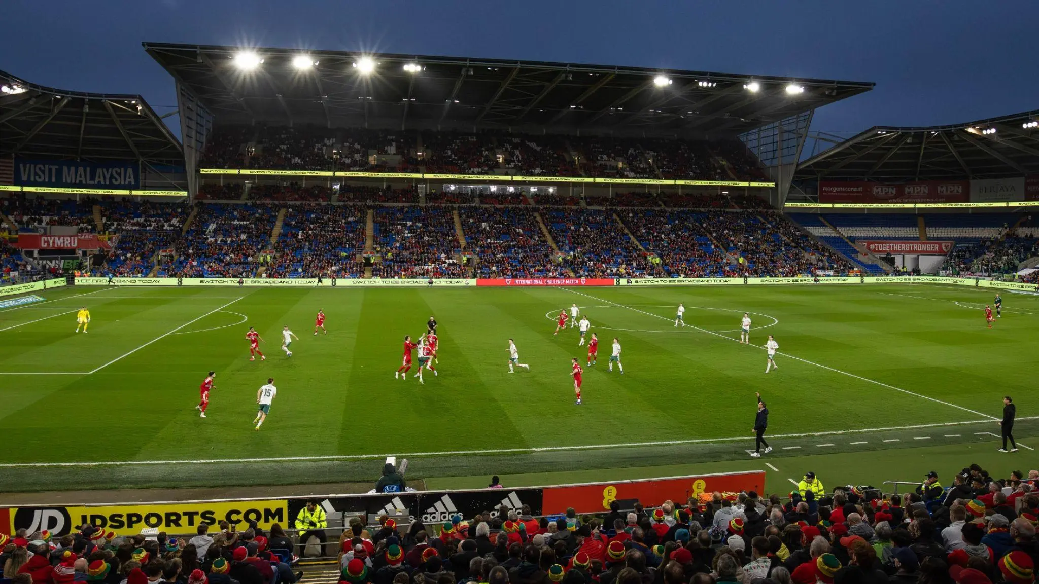 Wide shot of a professional football match under floodlights at Cardiff City Stadium with fans in the stands.