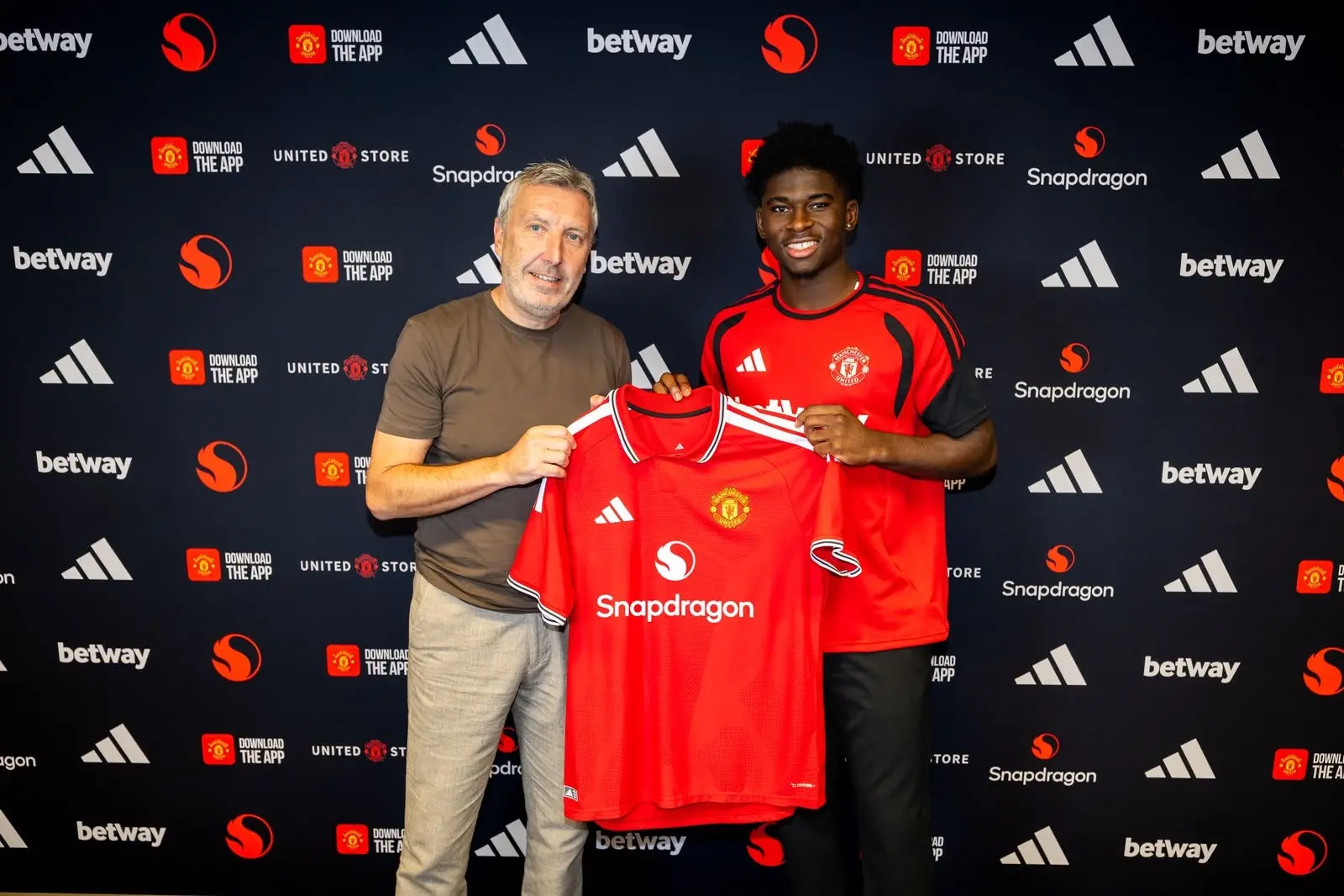 Carlos Baleba and a club official holding up a Manchester United home jersey during an official presentation