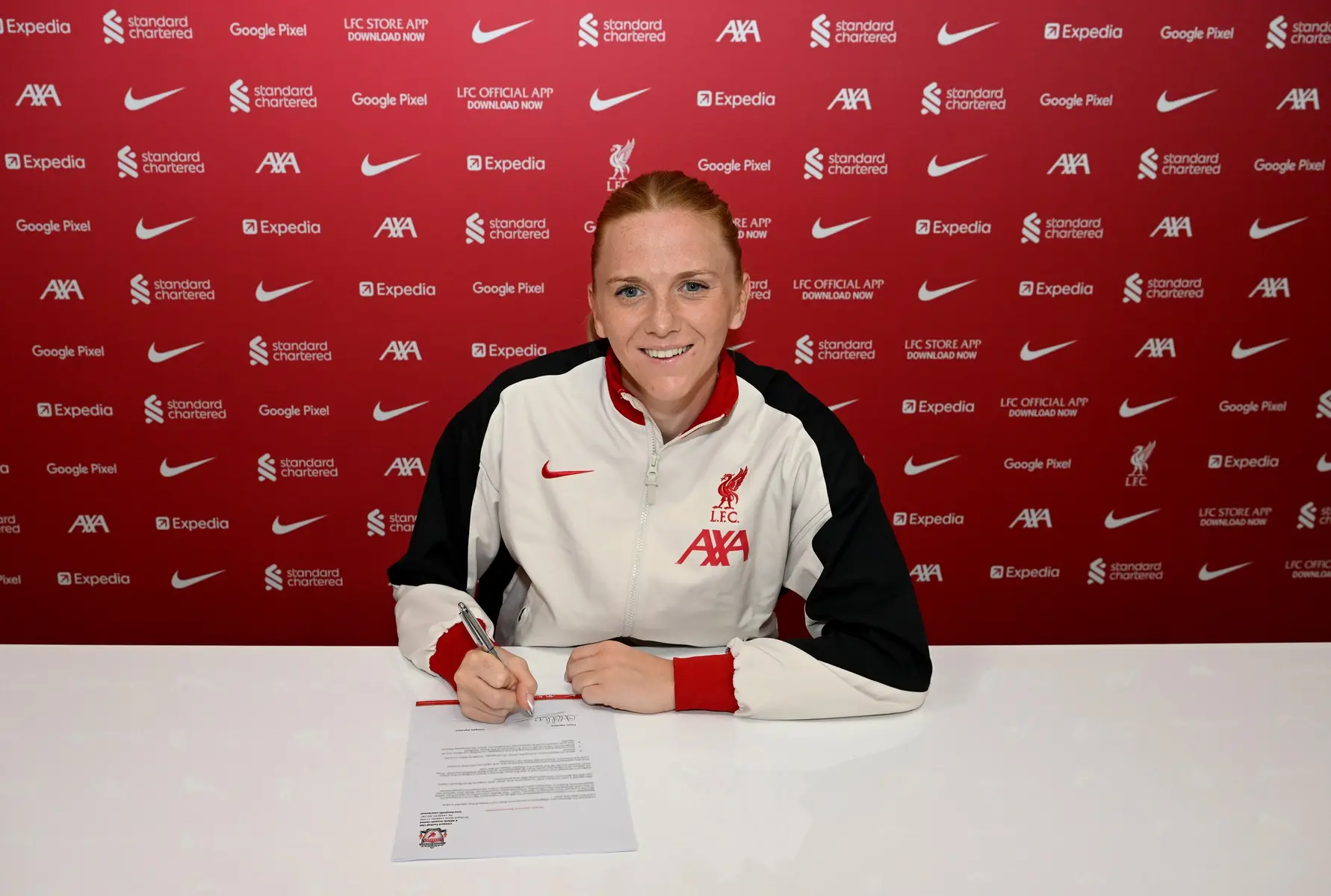 Ceri Holland wearing a Liverpool FC training jacket while signing a contract at a press conference