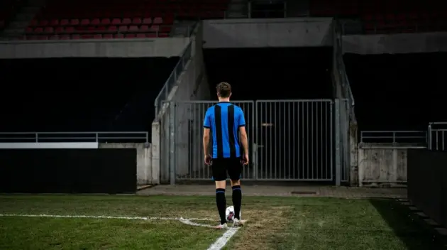 Young Club Brugge-inspired left-back beside a closed stadium gate during a transfer standoff