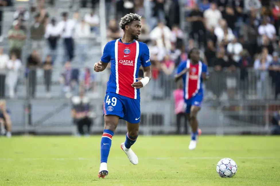 Ibrahim Mbaye in a Paris Saint-Germain kit dribbling a soccer ball on a grass field during a match