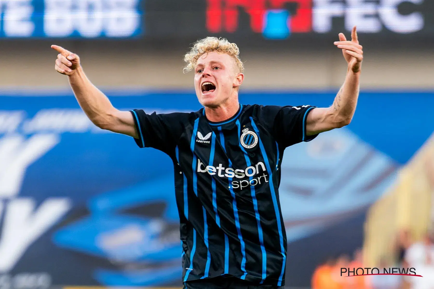 Joaquin Seys of Club Brugge celebrating with arms raised in a blue and black striped jersey.