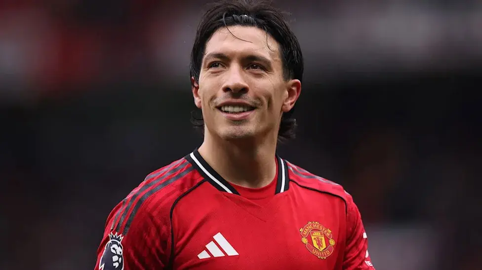Lisandro Martinez wearing the Manchester United home kit and smiling on the pitch