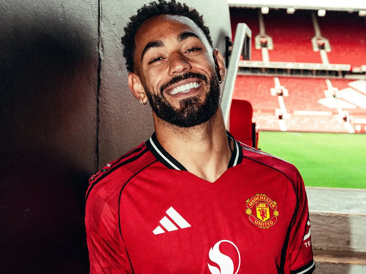 Matheus Cunha smiling in a red Manchester United home kit at Old Trafford stadium