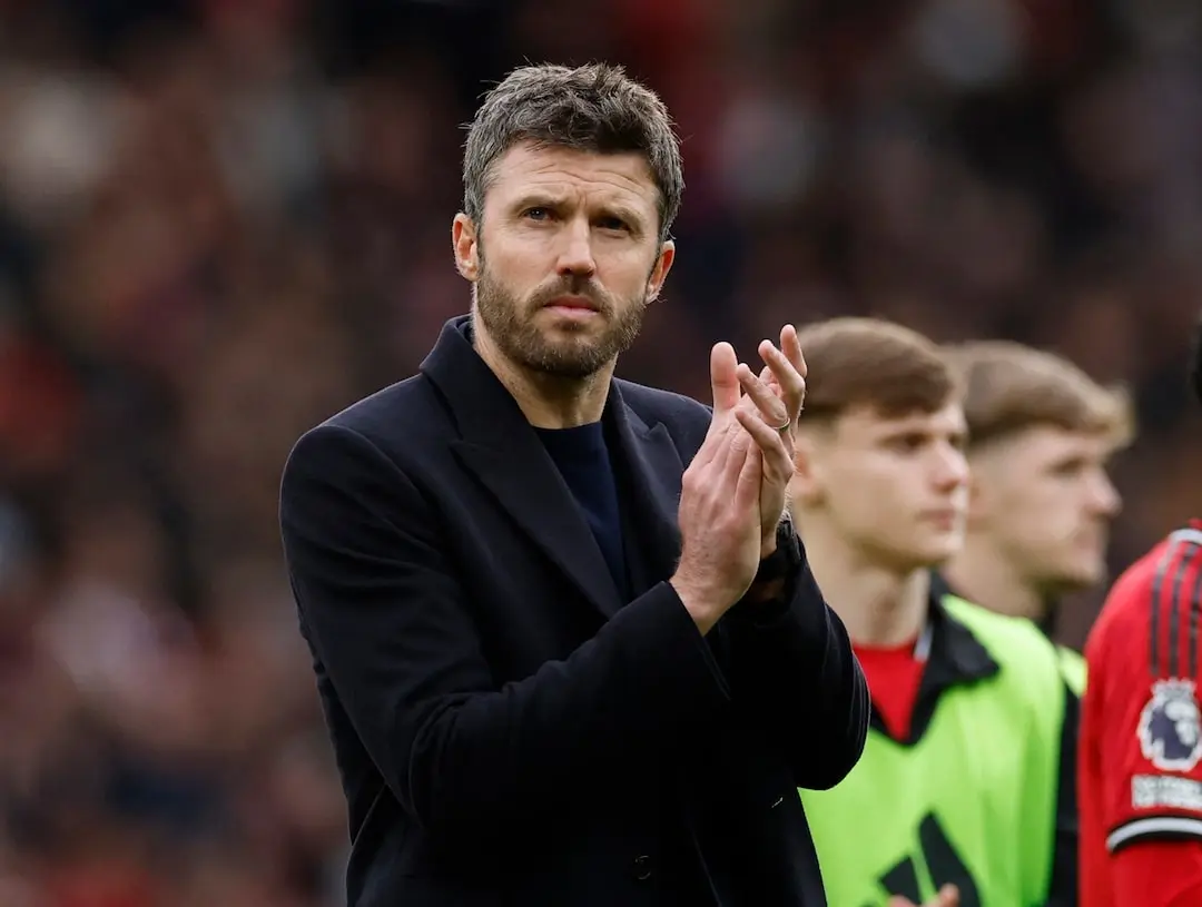 Michael Carrick wearing a dark coat and clapping at a football match