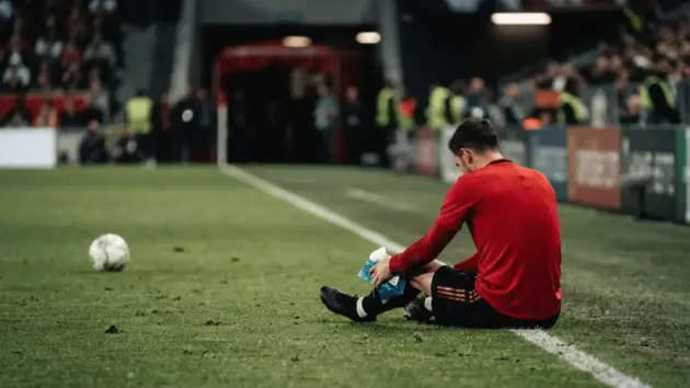 Injured football midfielder sits beside the pitch, symbolising Manchester United’s midfield transfer dilemma