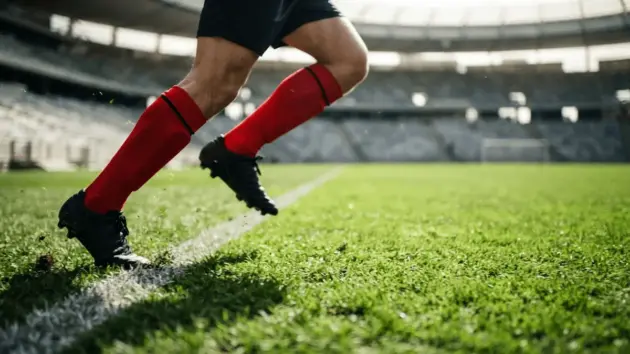 Football player sprinting down left flank in red socks on green pitch with dramatic lighting