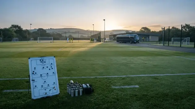 Empty training ground at dawn with tactical board and team bus ready for pre-season friendly departure