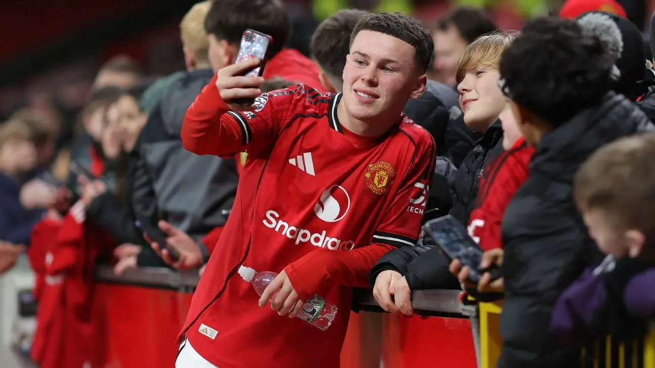 Kai Rooney in a Manchester United home kit taking a selfie with fans in the stadium