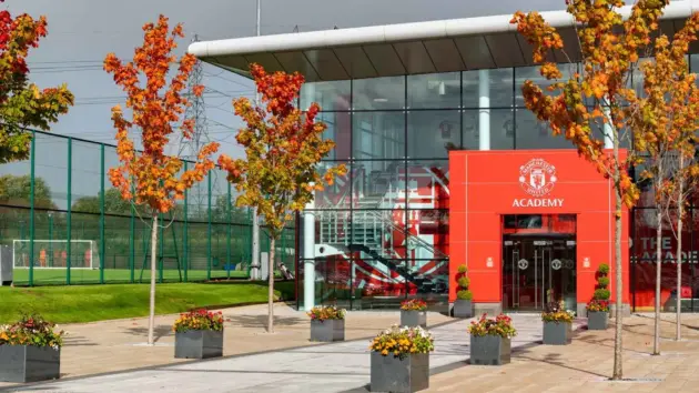 The exterior of the Manchester United Academy building with autumn trees and a rainbow in the sky