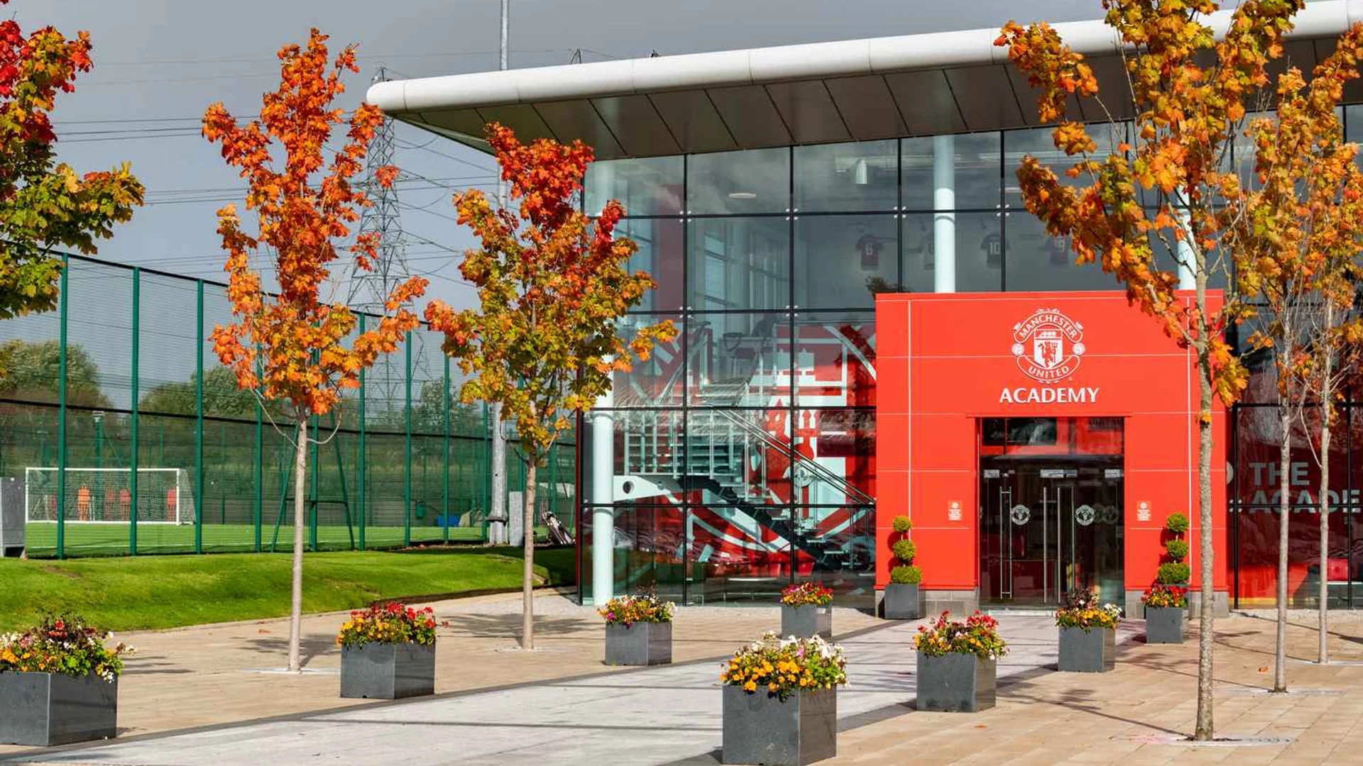 The exterior of the Manchester United Academy building with autumn trees and a rainbow in the sky