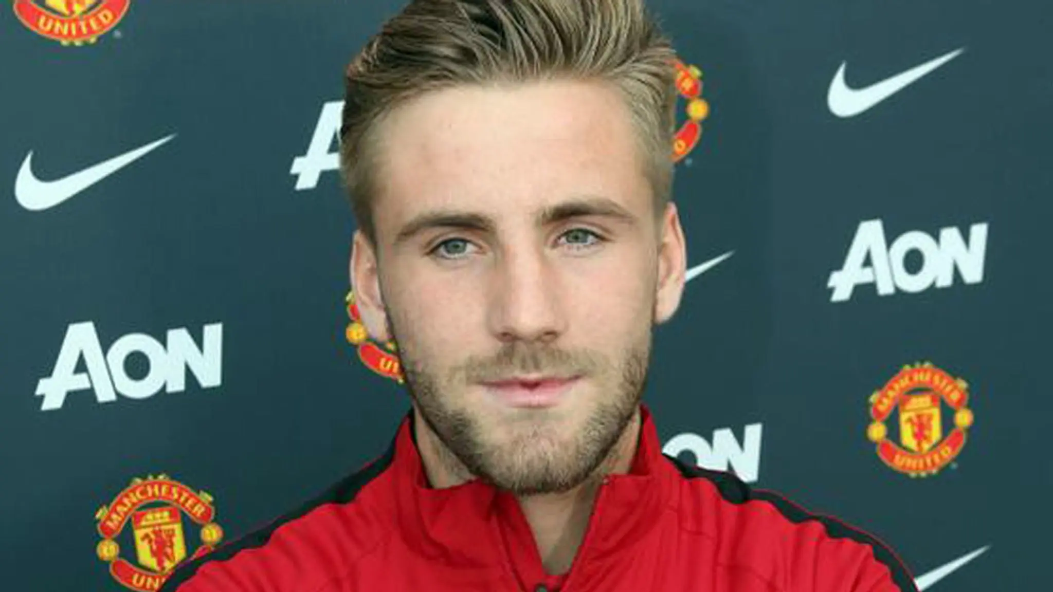Headshot of Luke Shaw wearing a red Manchester United training jacket against a branded backdrop.