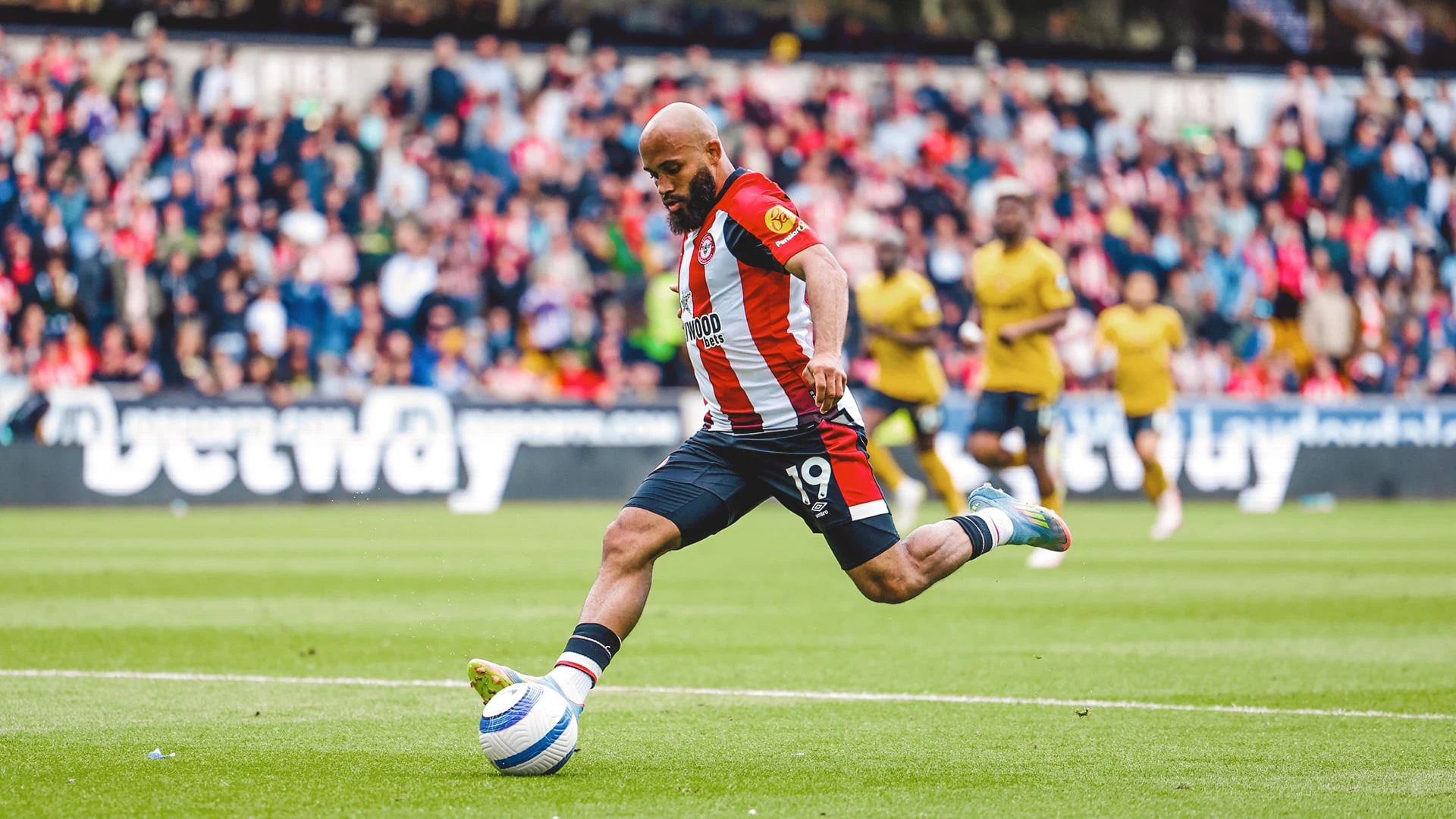 Bryan Mbeumo in a Brentford FC kit kicking a football during a match.