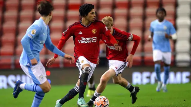 Manchester United Under-21 players in red kits competing for the ball against opponents in light blue kits.