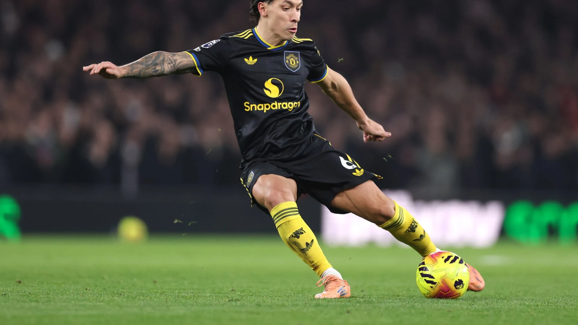 Lisandro Martínez in a black Manchester United kit playing the ball during a match.